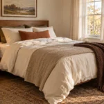 AI-created fall bedroom with cream bedding, a rust pillow, oatmeal coverlet and chocolate-brown throw against warm wood furniture.