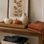 AI-created fall console with neutral pumpkins, a cream vase, autumn artwork and a rust throw; Halloween bat accents are packed in a box below.